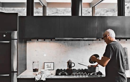 A man cooks in a modern, minimalist kitchen with a sleek marble backsplash. A small, discreet Josh Nano device is visible on the wall.